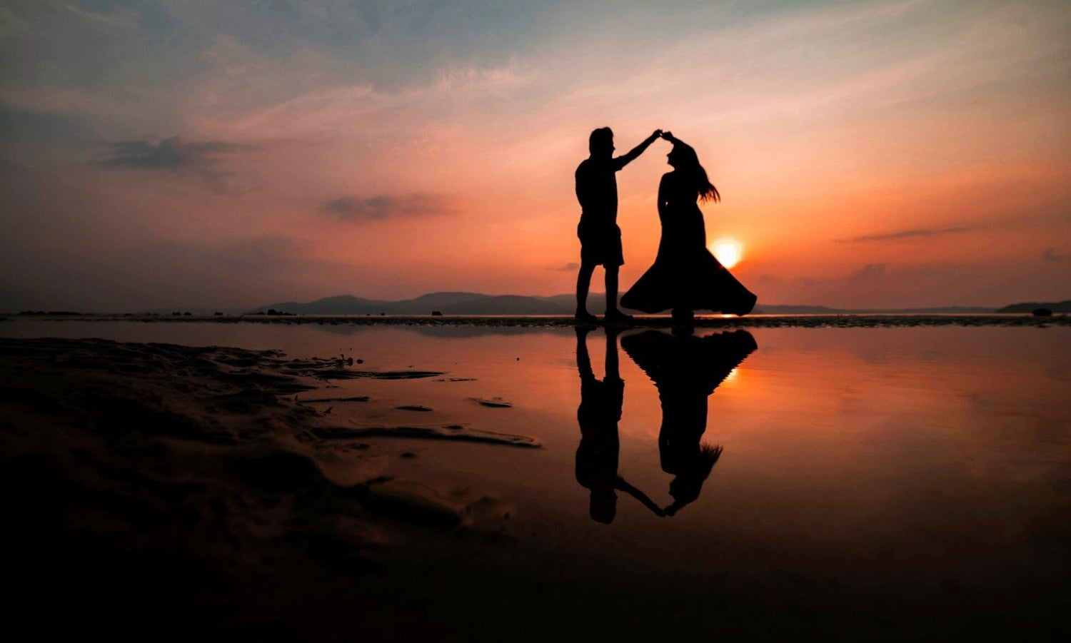 silhouette of couple dancing against sunset on beach